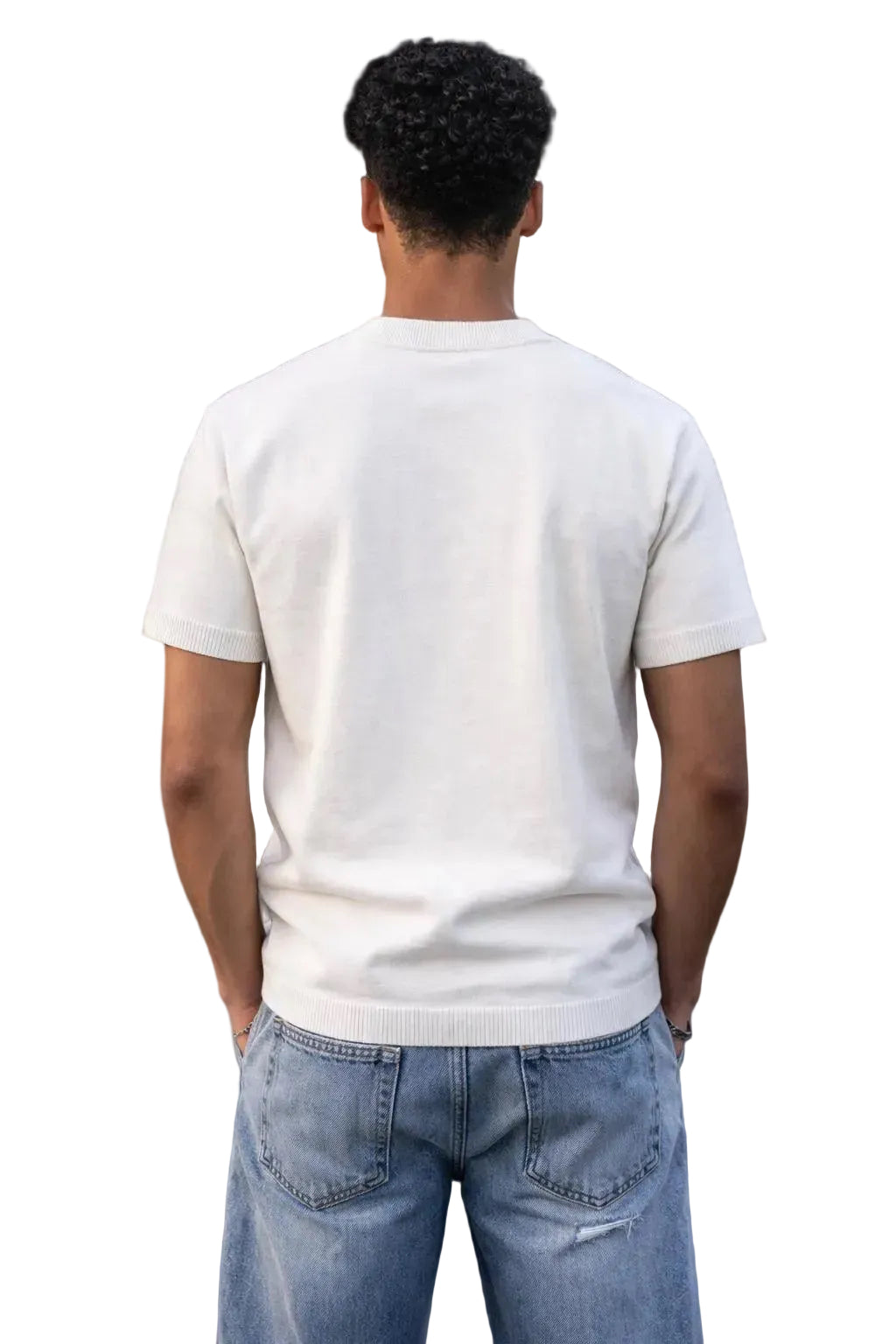 Back view of a man wearing an oversized off-white cotton knit short sleeve t-shirt with light wash jeans.