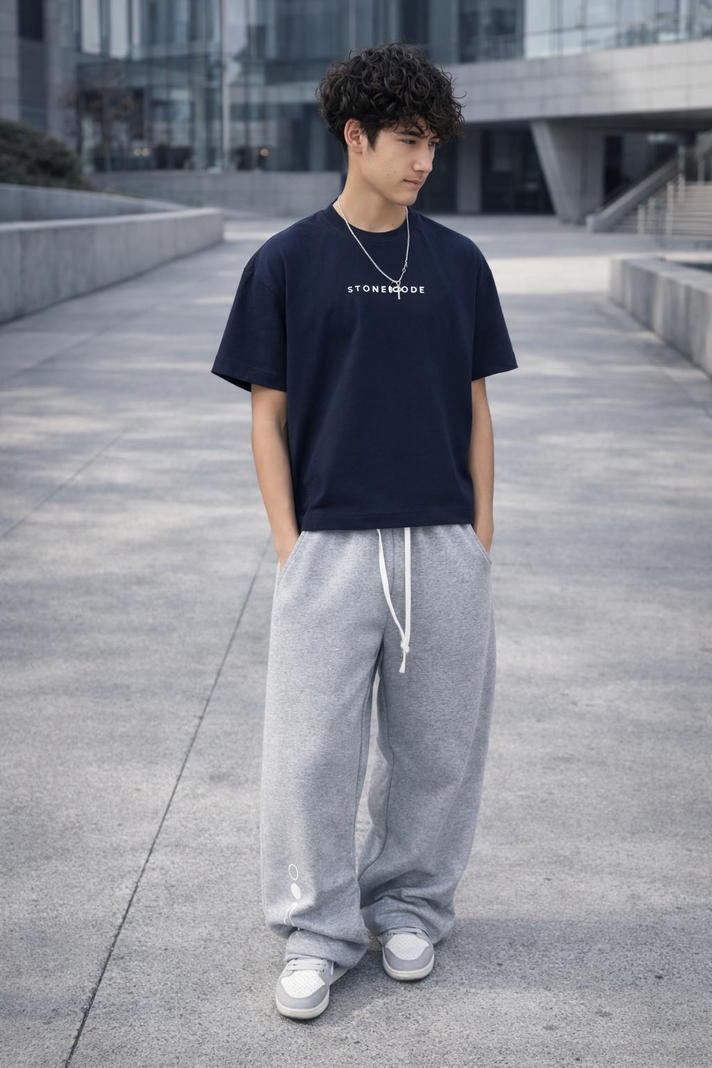 Young man wearing a navy blue Essential Cotton Boxy T-Shirt with white "STONEMODE" text and gray sweatpants.