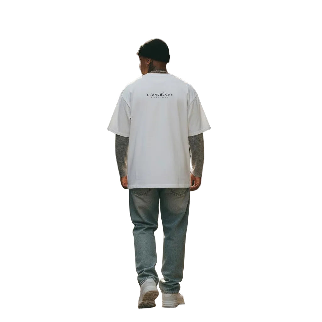 Unisex white pure cotton loose-fit t-shirt with "STONECODE" logo, worn over a grey long-sleeve shirt, paired with light wash jeans.