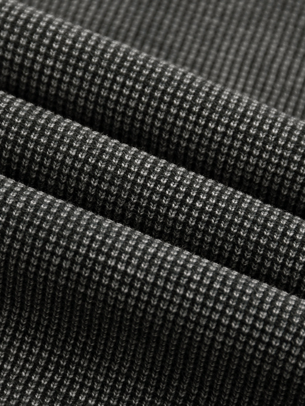 Close-up of a dark grey mineral wash waffle knit t-shirt fabric, showing its textured cotton blend.