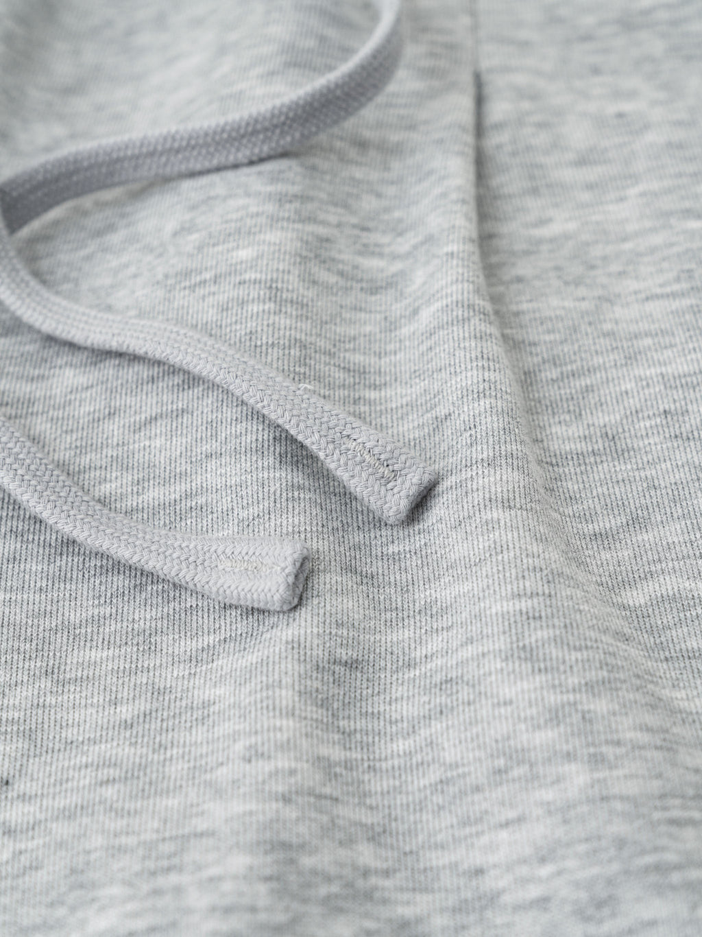 Close-up of light gray cotton-polyester blend fabric with a drawstring, showing texture.