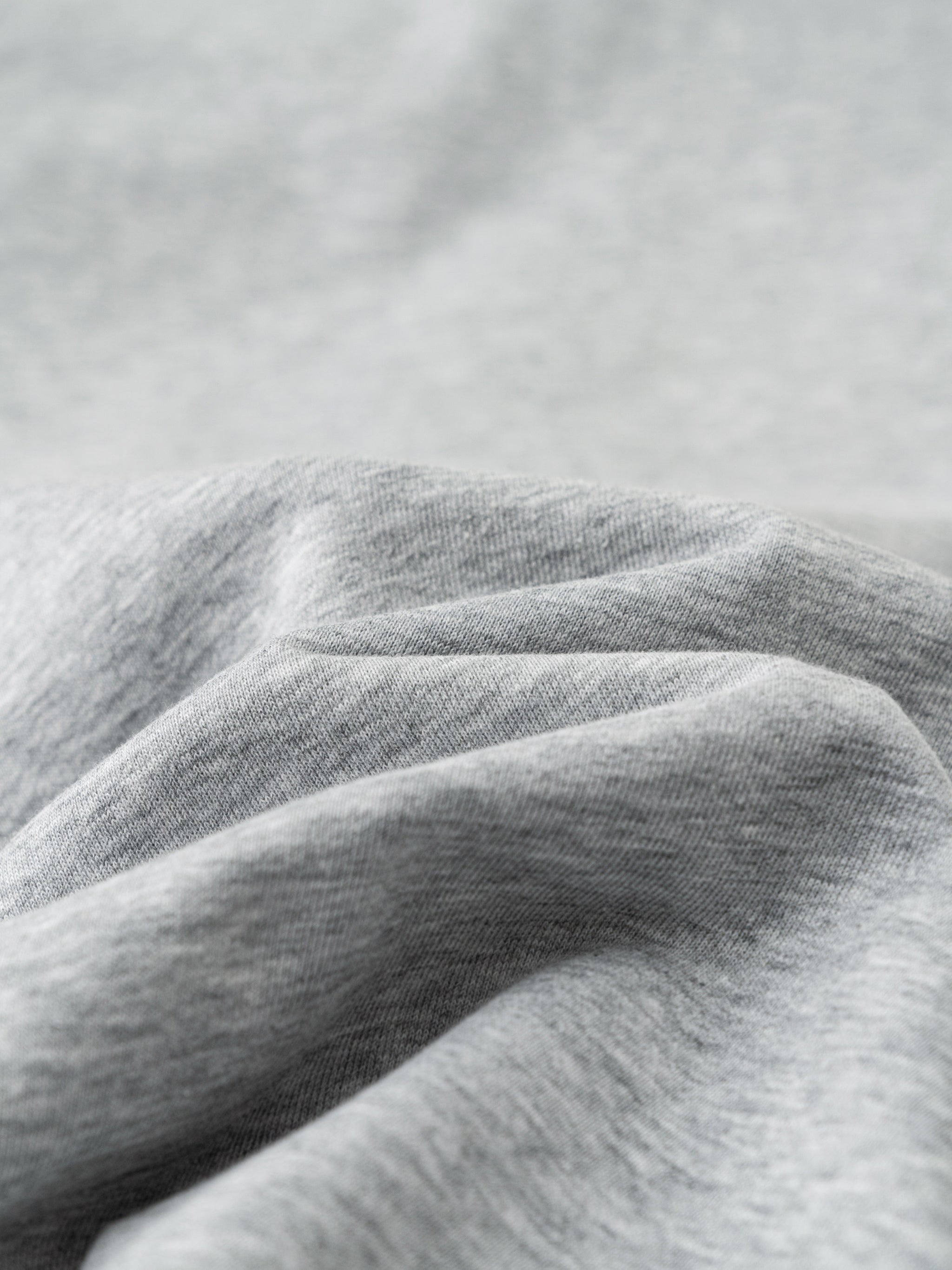 Close-up of soft, light gray cotton-polyester blend fabric with gentle folds, ideal for casual pants.