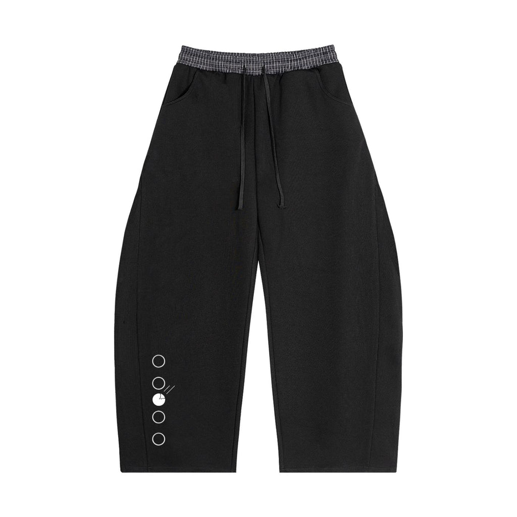 Black barrel sweatpants with a plaid waistband, drawstring, pockets, and decorative metal rings on the left leg.