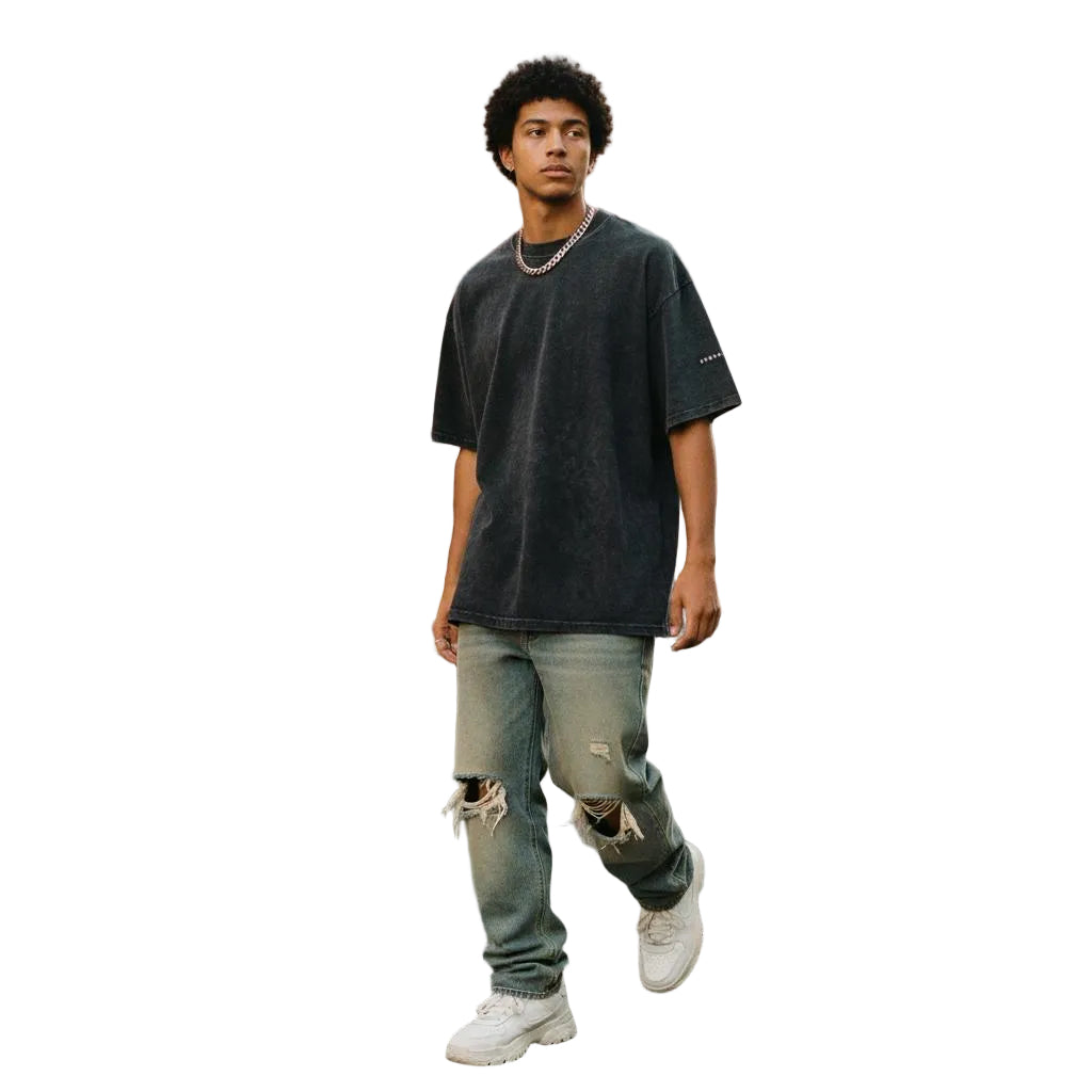 Man in a dark gray snow-washed oversized cotton t-shirt, ripped jeans, and white sneakers walking on a city street.