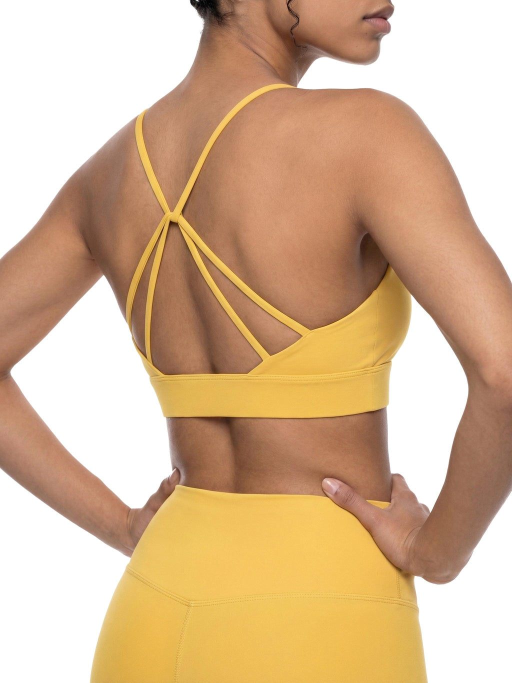 Yellow strappy criss-cross yoga sports bra and matching leggings on a model's back.