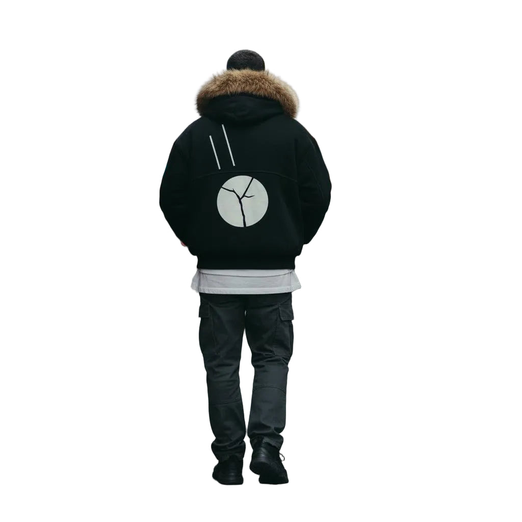 Unisex black boxy hoodie with detachable fur trim and white circular graphic, worn by a person walking down a city street.