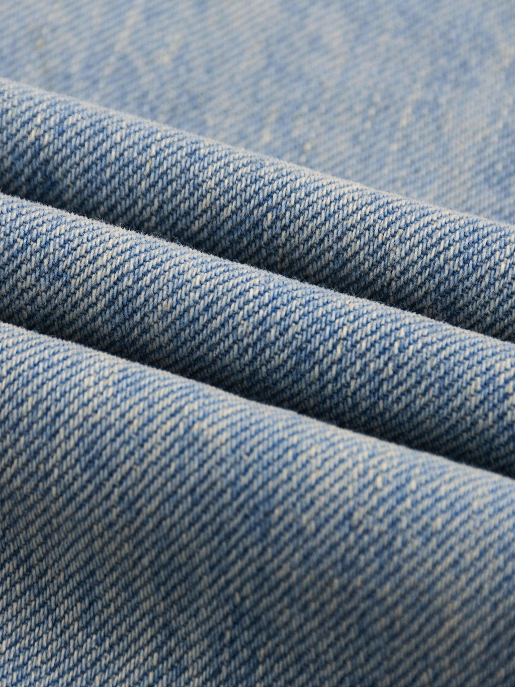 Close-up of sun fade raw hem denim jeans fabric, showing blue washed texture and weave.