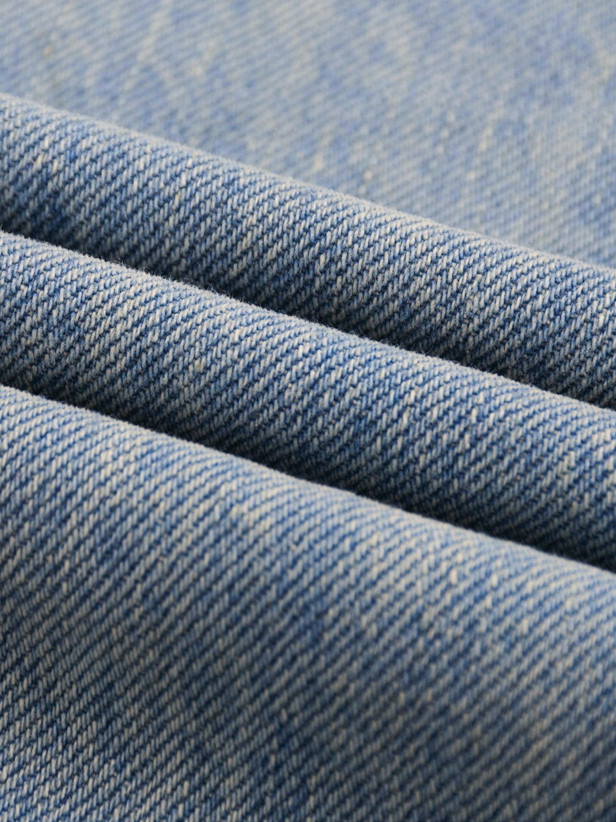 Close-up of sun fade raw hem denim jeans fabric, showing blue washed texture and weave.