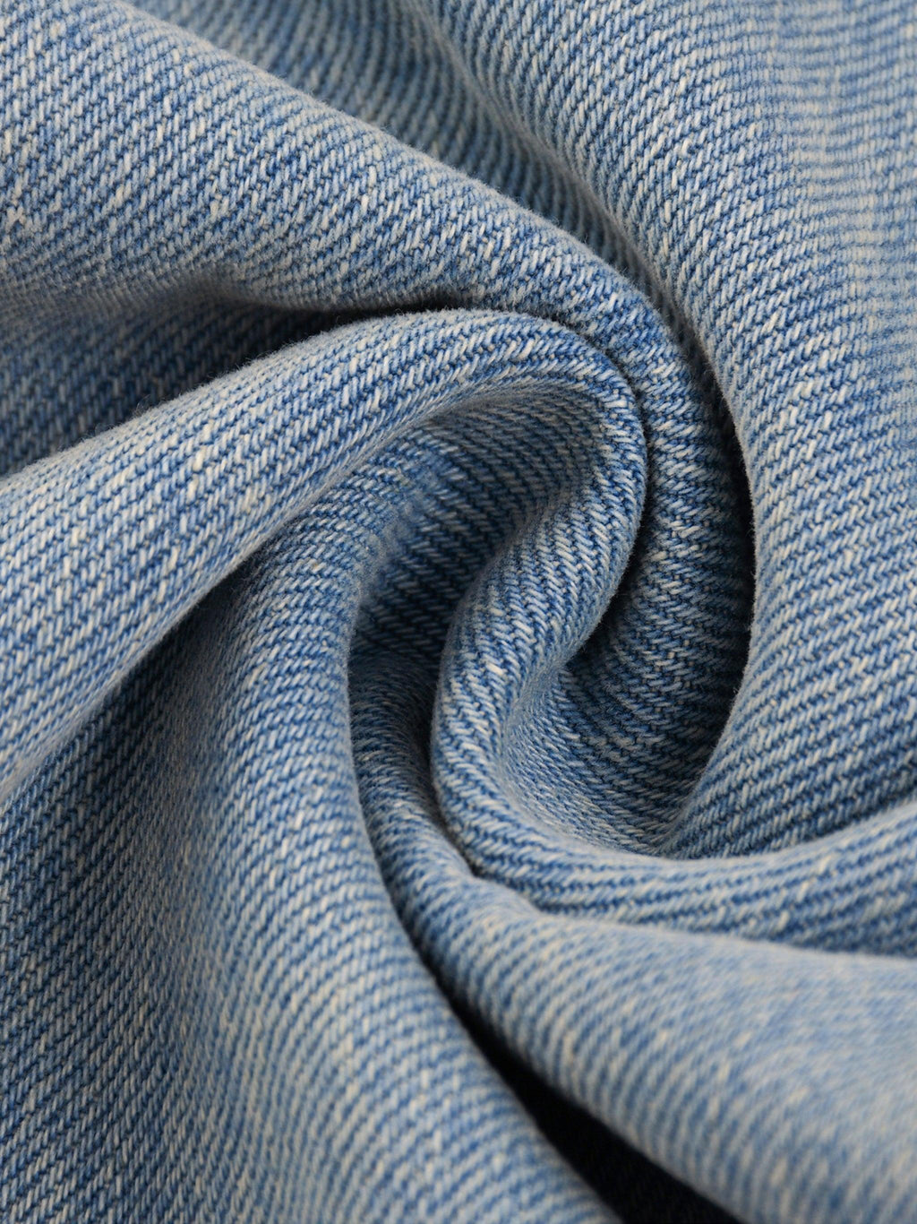 Close-up of sun fade raw hem denim jeans fabric, showing blue washed texture and weave.