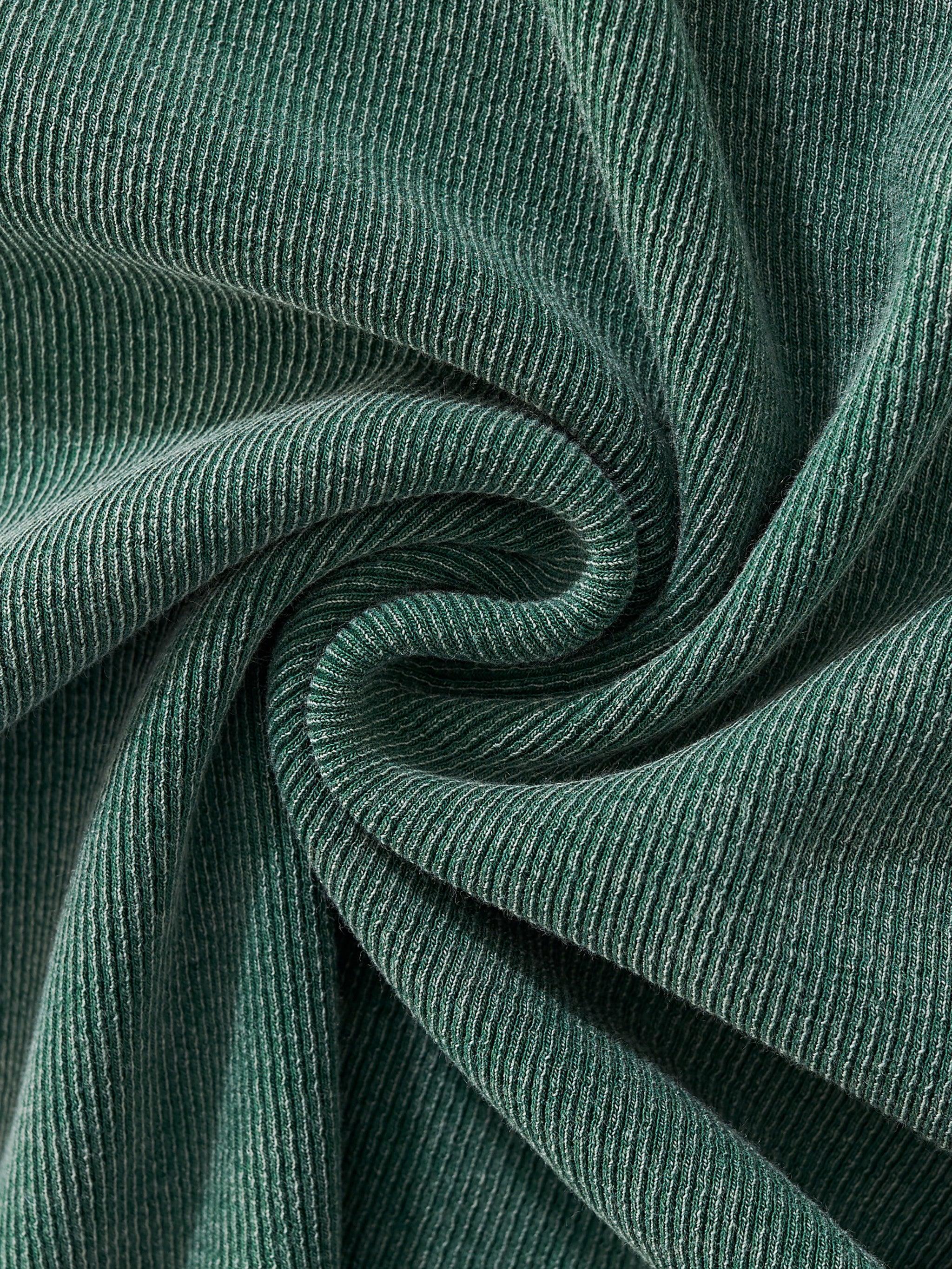 Close-up of a vintage washed, ribbed dark green cotton blend fabric with soft folds.