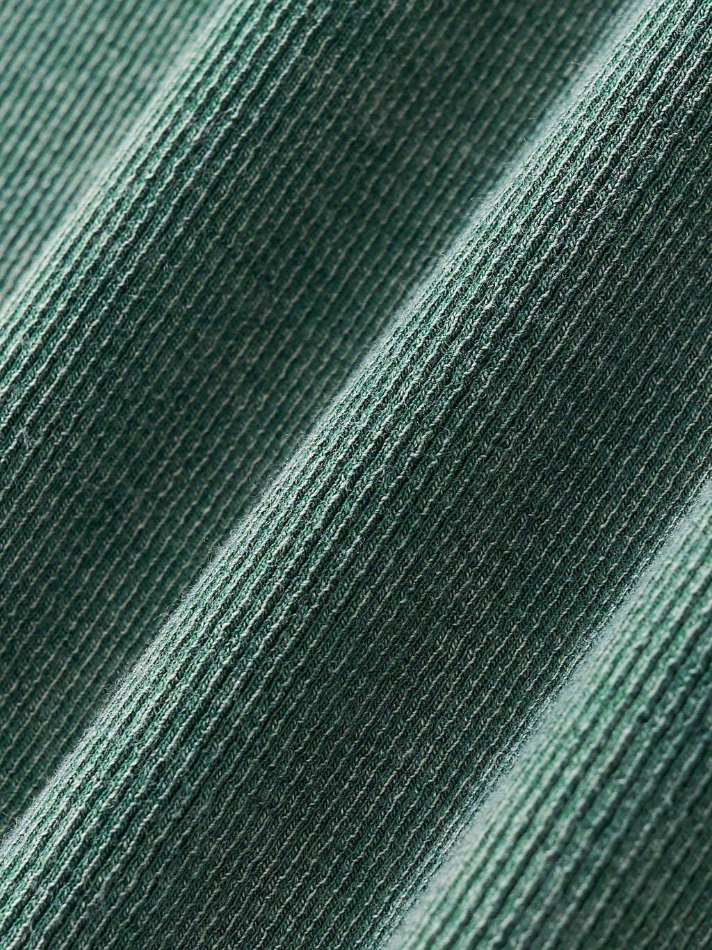 Close-up of a vintage washed, ribbed cotton blend fabric in a deep green color, showing texture and folds.