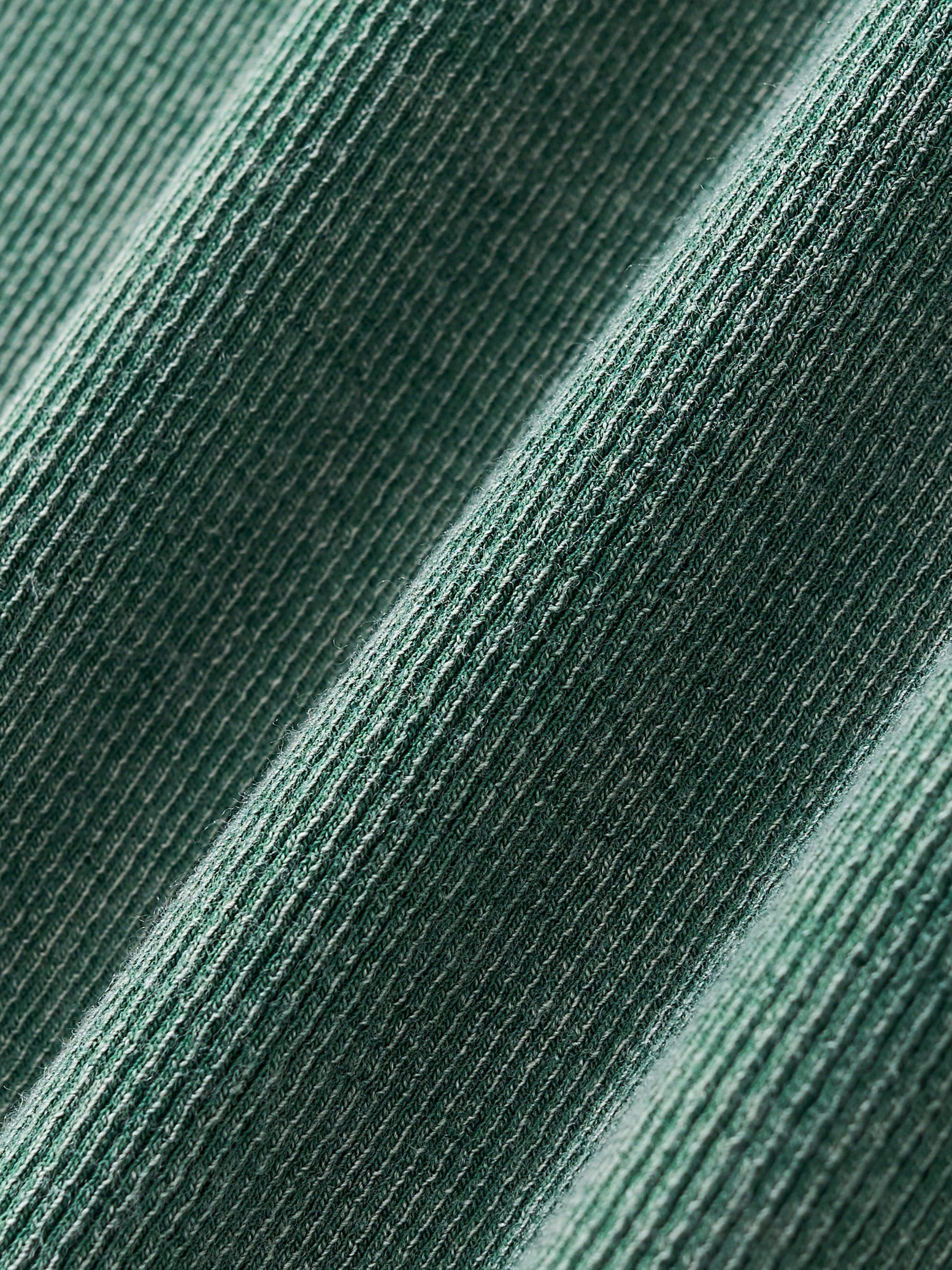 Close-up of a vintage washed, ribbed cotton blend fabric in a deep green color, showing texture and folds.
