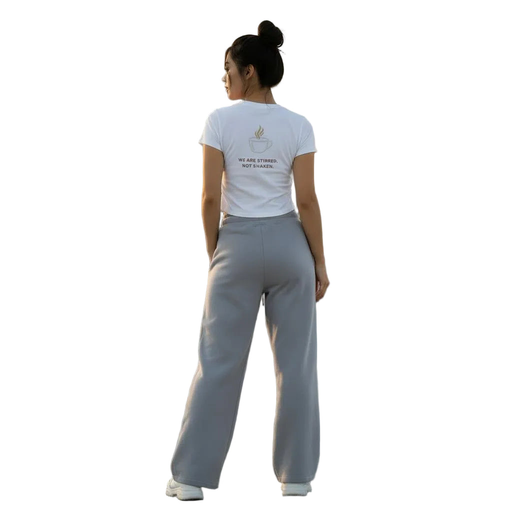 Woman in white crop top with coffee graphic and gray wide-leg sweatpants on a city rooftop at sunset.